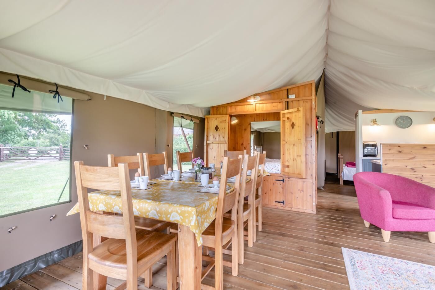 Un hébergement sous tente comprenant un espace repas, des meubles en bois et une chaise rose.