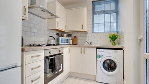 A compact kitchen with white cabinets, a microwave, a kettle, an oven, and a front-loading washing machine. - 1 Bed in Mumbles (oc-hh72) (The Mumbles)