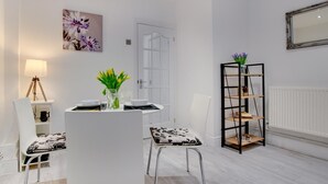 A modern dining area with a white table set for two, a vase of yellow tulips, and a black metal bookshelf. - 1 Bed in Mumbles (oc-hh72) (The Mumbles)