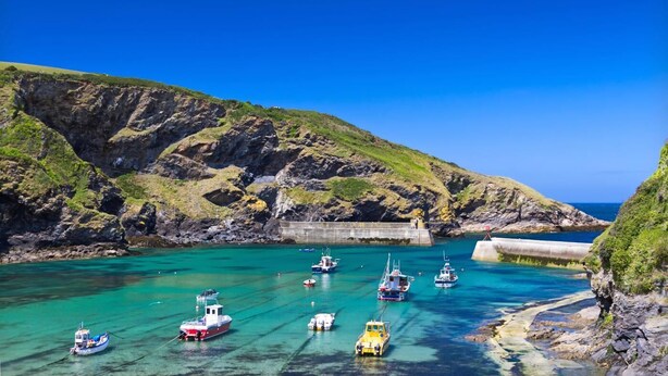 A coastal area with boats docked at a pier, surrounded by rocky cliffs and clear blue water. - 2 Bed in Bodmin (oc-p00429) (Saint Teath)