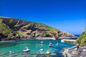 A coastal area with boats docked at a pier, surrounded by rocky cliffs and clear blue water. - 2 Bed in Bodmin (oc-p00429) (Saint Teath)