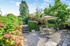 Une terrasse aménagée dans un jardin, avec une table et des chaises, entourée de gravier et de verdure.
