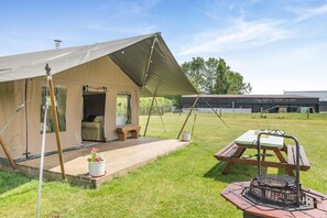 Eine Unterkunft in einem Zelt mit einer Terrasse, einem Picknicktisch und einem Grill.