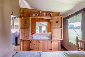 Ein Zeltraum mit Bett, Holzschränken und Blick ins Freie.