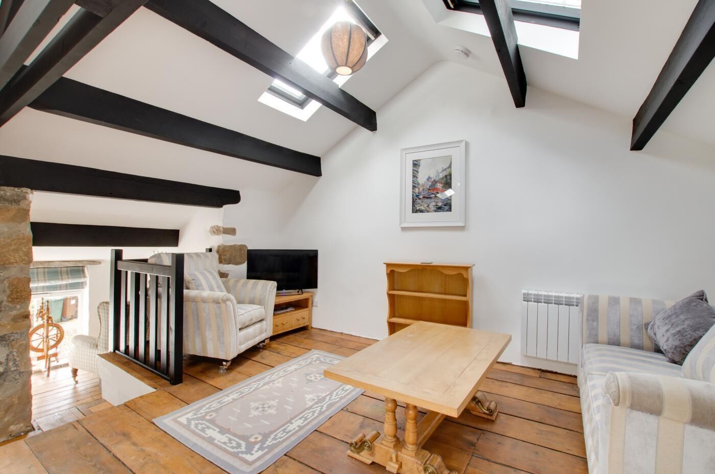 Een loft-woonkamer met zichtbare balken, een houten tafel, een bank, een televisie en een boekenplank.