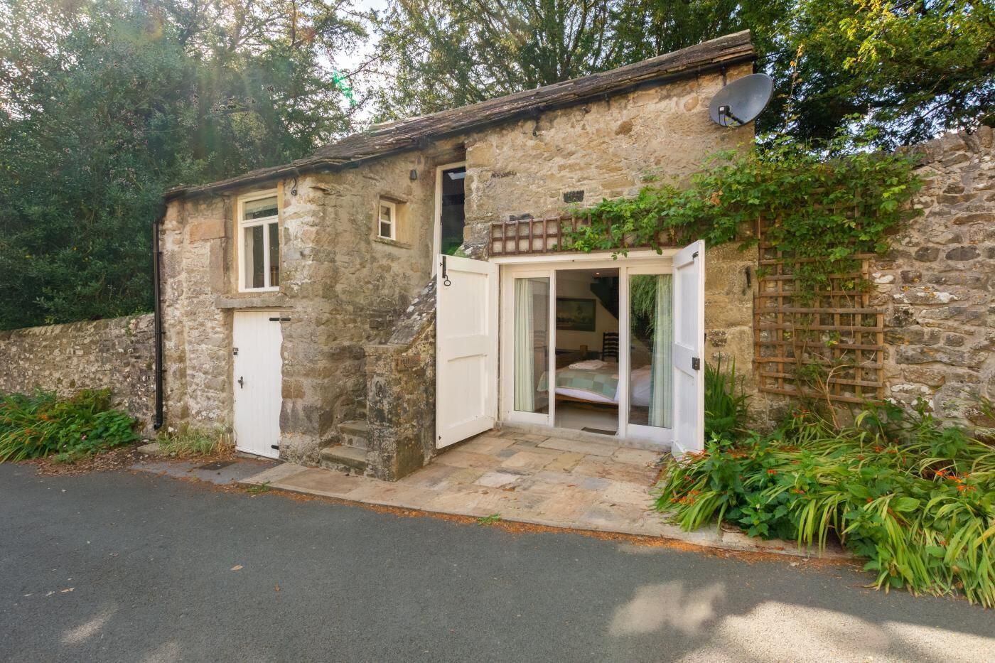 A stone building with a single door and a small window, a satellite dish on the roof, and a garden area with plants.