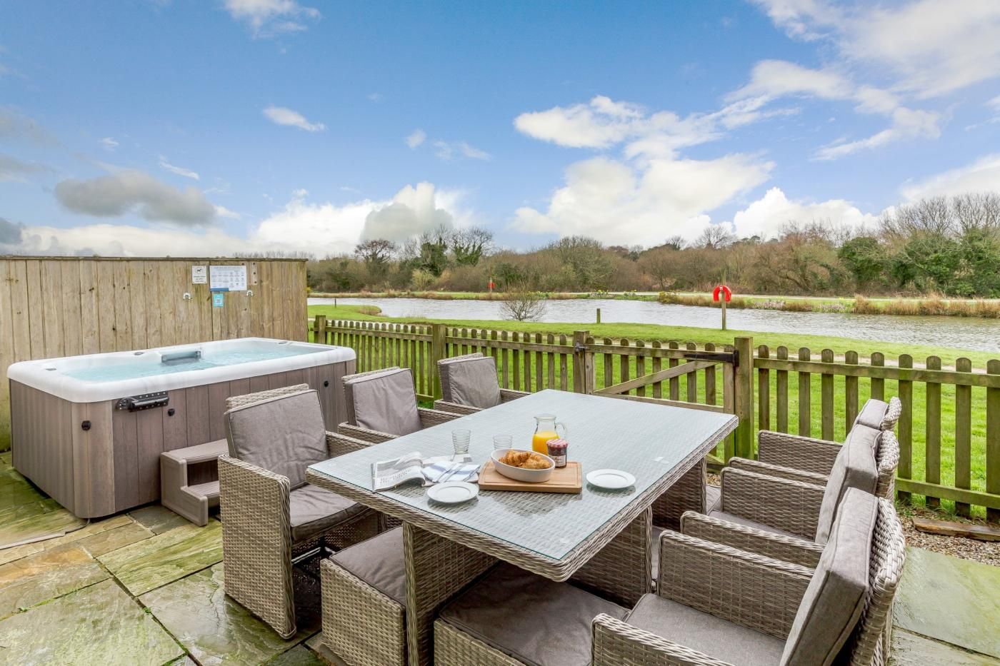 An outdoor patio with a hot tub, wicker furniture, and a table set for breakfast.