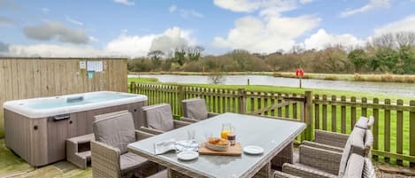 An outdoor patio with a hot tub, wicker furniture, and a table set for breakfast.