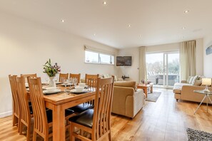 A spacious living area with a wooden dining table set for four, a sofa, and a television mounted on the wall. - 4 Bed in St Columb (oc-p00498) (Saint Wenn)