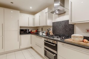 A modern kitchen with white cabinets, a granite countertop, a gas stove, a microwave, and a toaster. - 4 Bed in St Columb (oc-p00498) (Saint Wenn)