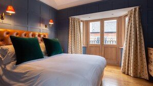 Een slaapkamer met een groot bed, twee wandlampen, een houten hoofdbord en uitzicht door een deur.