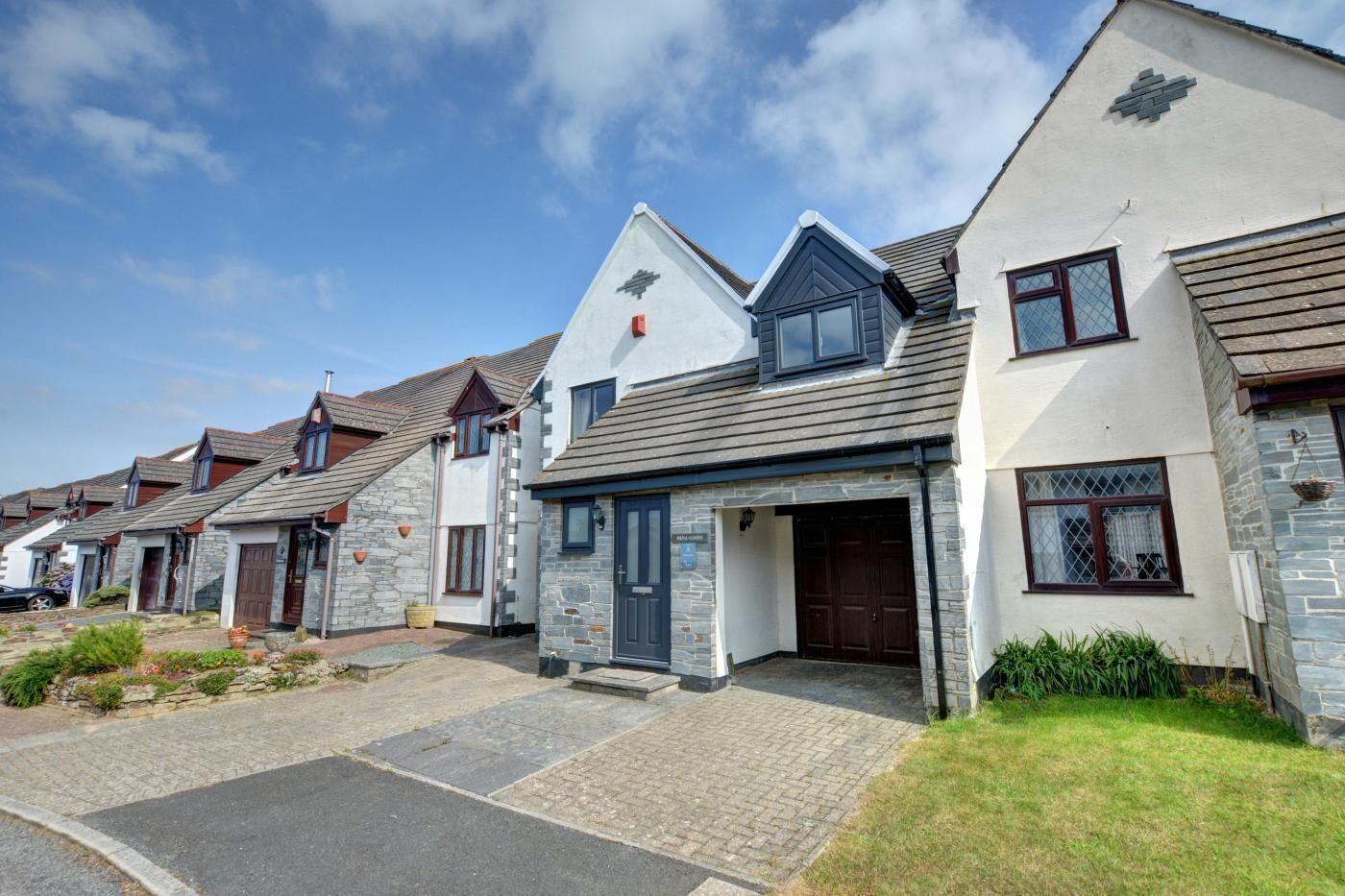 A row of modern houses with stone facades, a driveway, and a clear sky.