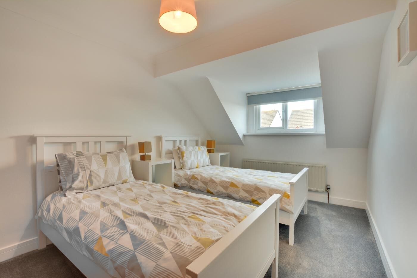 A bedroom with two beds, a window, a radiator, and a ceiling light.