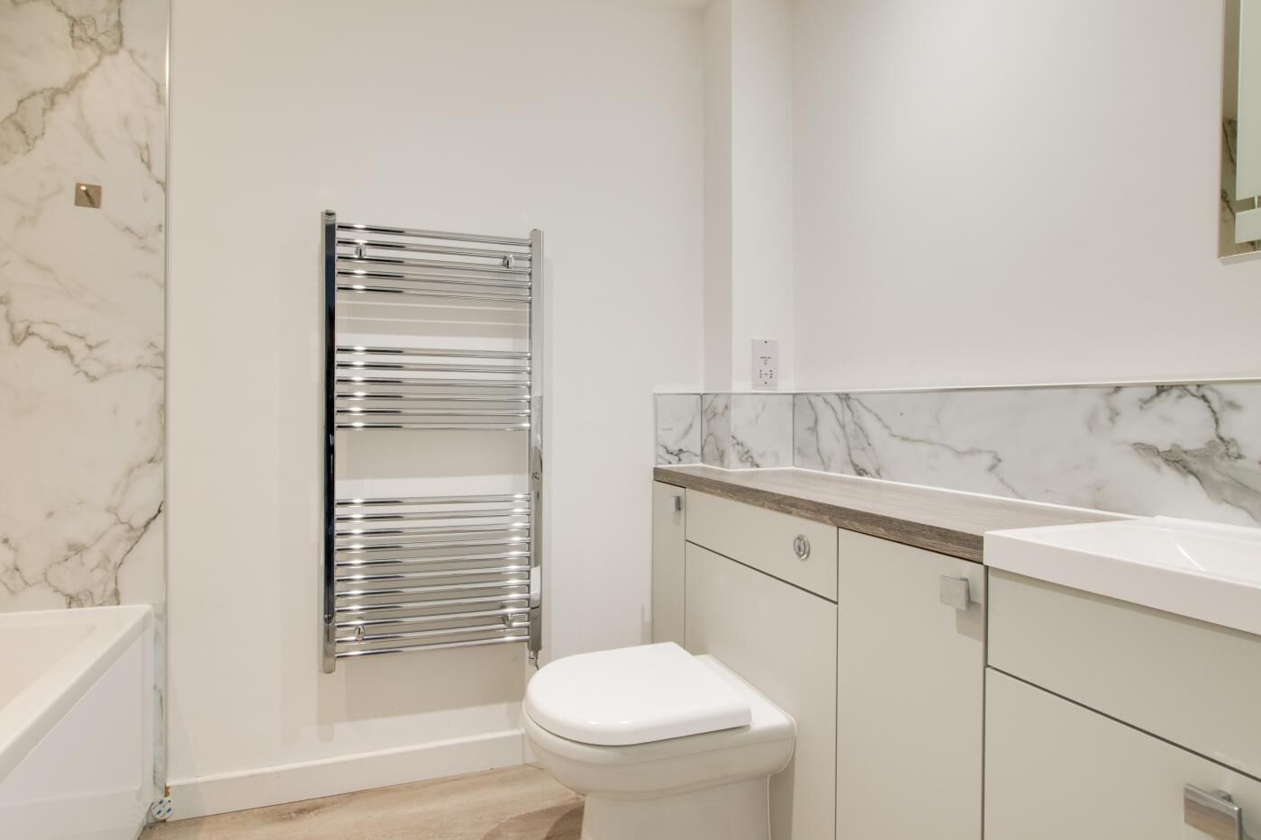 A modern bathroom with a marble backsplash, a chrome towel rack, a white toilet, and a wooden vanity.