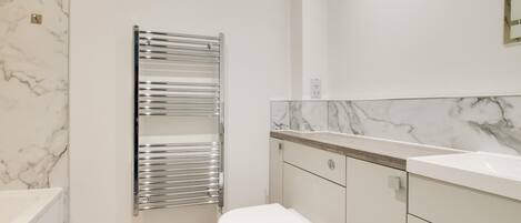 A modern bathroom with a marble backsplash, a chrome towel rack, a white toilet, and a wooden vanity.