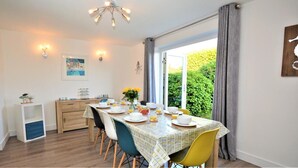 Un coin repas avec une table dressée pour quatre personnes, un buffet en bois et une vue sur la verdure à l’extérieur.