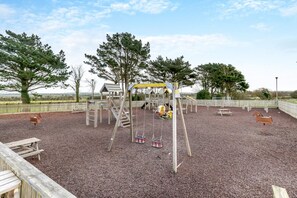 A playground with wooden structures, swings, and a slide. - 2 Bed in Padstow (oc-p00155) (Penrose)