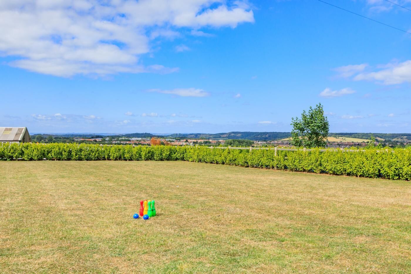 A grassy field with a fence, a tree, and a distant building.