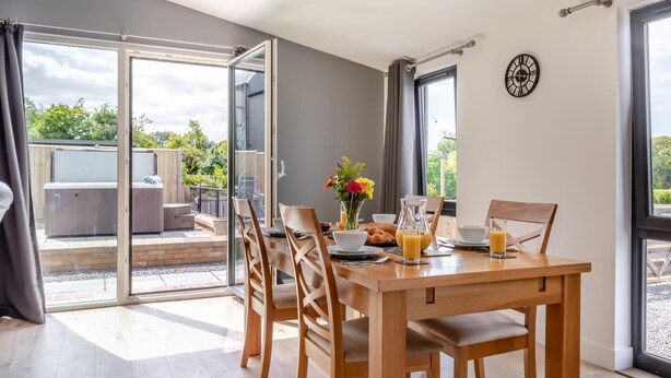A dining area with a table set for breakfast, a hot tub outside, and a clock on the wall. - 2 Bed in Somerton (oc-s32606) (Windy Ridge)