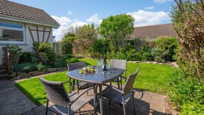 Une terrasse avec une table ronde et quatre chaises, entourée d’un jardin bien entretenu et d’une maison avec un toit en tuiles.