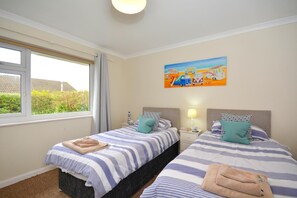 Ein Doppelzimmer mit zwei Betten, einem fenster mit Vorhängen, einem Bild an der Wand und Blick auf Grün.