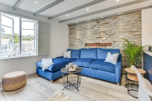 Ein modernes Wohnzimmer mit einem blauen Sofa, einer Steinwand und Blick auf die Stadt.