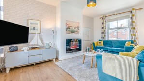 A modern living room with a flat-screen TV, a fireplace, a blue sofa, and a white brick wall. - 3 Bed in Padstow (oc-p00878) (Padstow)