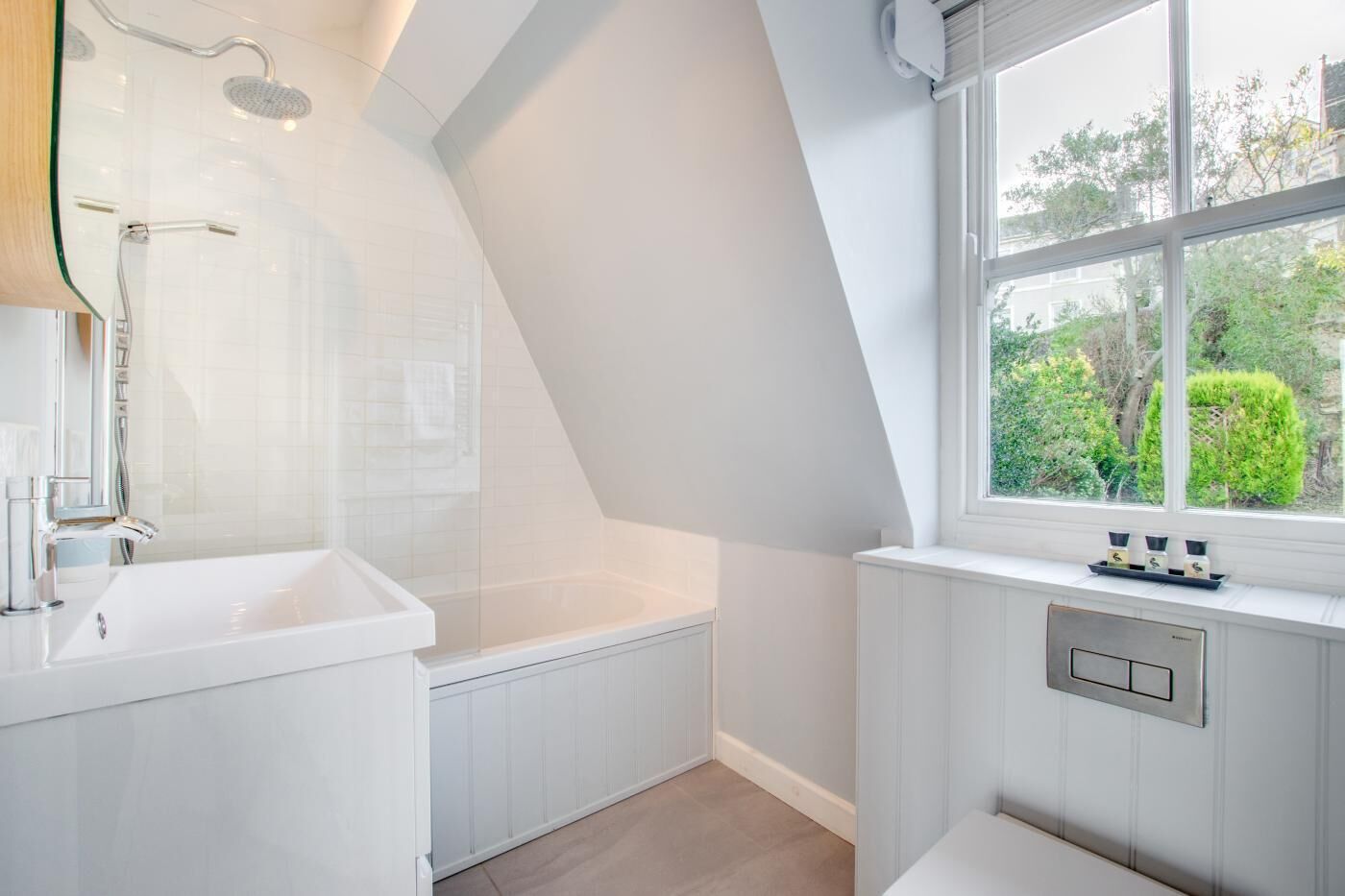 Ein modernes Badezimmer mit einer freistehenden Badewanne, einer Duschkabine aus Glas und einem Fenster mit Blick ins Grüne.