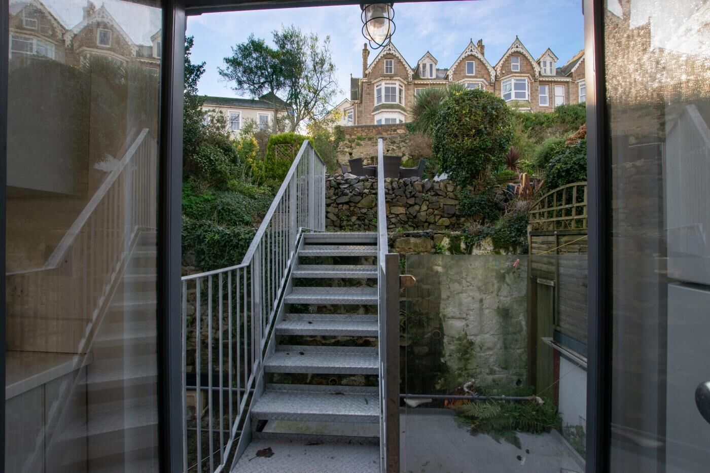 Eine Treppe führt zu einer Steinmauer, mit Blick auf ein großes, historisches Gebäude im Hintergrund.