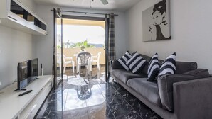 A modern living room with a grey sofa, a flat-screen TV, and a ceiling fan. - Castle Harbour 2 Bed Duplex (Los Cristianos)