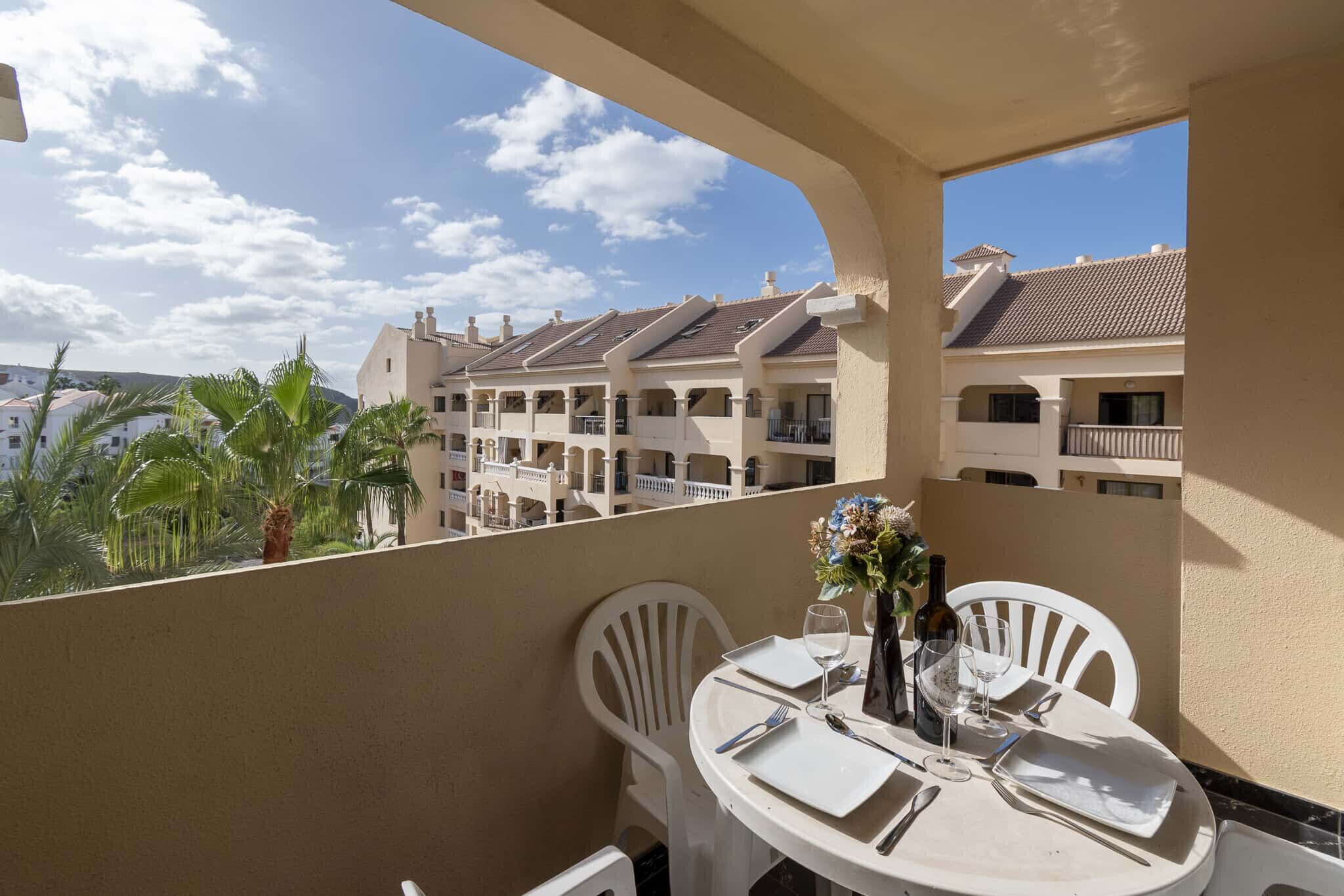 A balcony with a table set for two, overlooking a row of buildings with balconies.