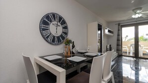 A dining area with a black and white clock, white chairs, and a glass table. - Castle Harbour 2 Bed Duplex (Los Cristianos)