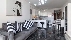 A modern living room with a grey sofa, black and white striped pillows, and a black and white abstract painting on the wall. - Castle Harbour 2 Bed Duplex (Los Cristianos)