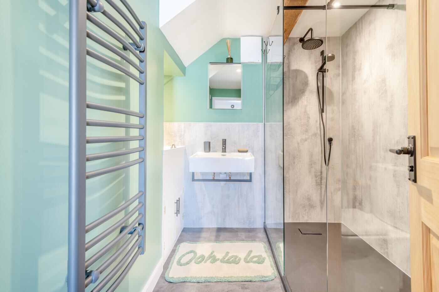 Un baño moderno con cabina de ducha de vidrio, un lavamanos con espejo y un perchero.