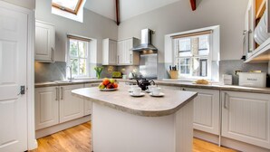 A modern kitchen with a central island, white cabinetry, a gas stove, and a skylight. - 4 Bed in Padstow (oc-p00011) (Padstow)