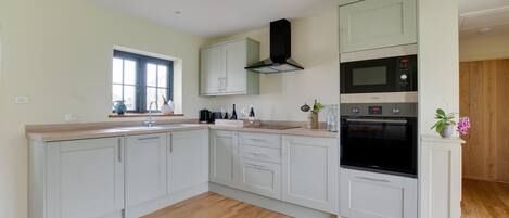 A modern kitchen with light-colored cabinets, a built-in oven, and a window providing natural light.