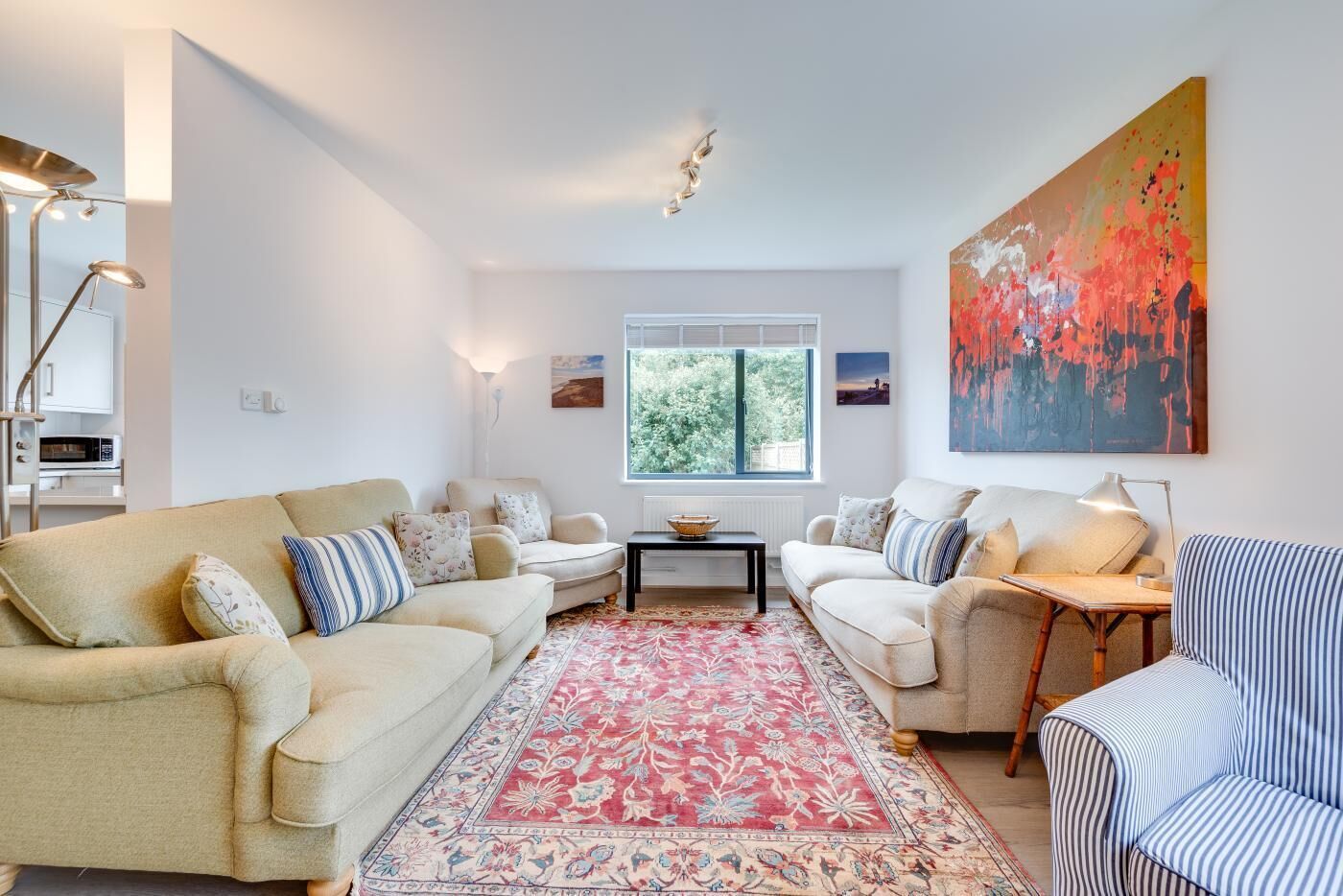 Un salon avec deux canapés, une table basse, un tapis à motifs, un tableau et une fenêtre donnant sur des arbres.