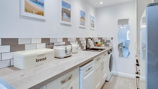 Una cocina moderna con armarios blancos, salpicadero de azulejos y lavavajillas integrado.