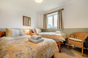 A double room with two beds, a chair, a mirror, and a window with curtains. - 3 Bed in Padstow (oc-p00105) (Saint Merryn)