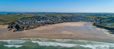 An aerial view of a coastal town with a sandy beach, clear blue waters, and a residential area with houses.