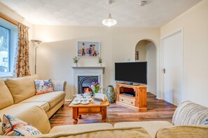 A living room with a sofa, a coffee table with teacups, a fireplace, a TV, and a large window. - 3 Bed in Padstow (oc-p00105) (Saint Merryn)