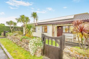 Ein Haus mit Steinmauer, Holztor und Garten mit Blumen und Pflanzen.