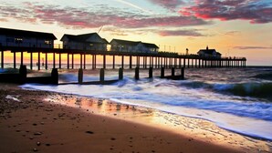 Eine Pier mit Gebäuden, die sich ins Wasser erstrecken, ein Sandstrand und Wellen, die an die Küste brechen.