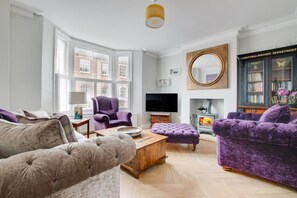 A modern living room with a fireplace, a television, and a bookshelf. - 5 Bed in Southwold (oc-tlw) (Southwold)