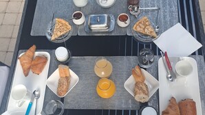 Een ontbijt opstelling op een tafel met croissants, brood en gebak, inclusief een kleine vaas met bloemen.