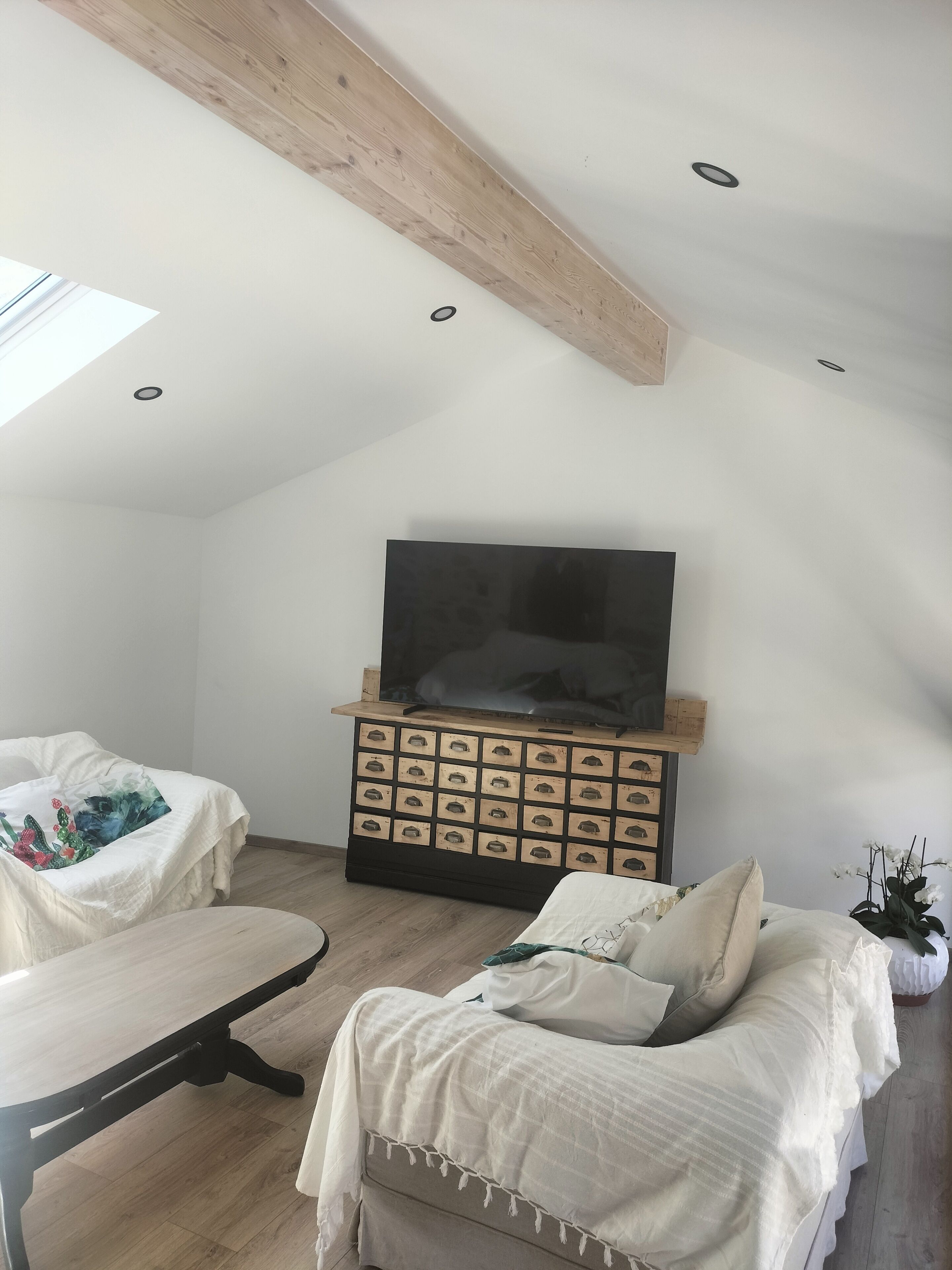 Une chambre à coucher confortable, aménagée en mezzanine, avec un plafond en pente, un grand téléviseur à écran plat fixé sur un meuble en bois, un lit avec une literie blanche et un banc agrémenté d’un coussin.