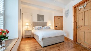 A bedroom with a bed, bedside tables, a wooden wardrobe, and a wall decoration. - 2 Bed in Padstow (oc-p00505) (Padstow)