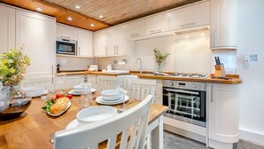A modern kitchen with white cabinets, a wooden countertop, and a dining table set for four. - 2 Bed in Padstow (oc-p00505) (Padstow)