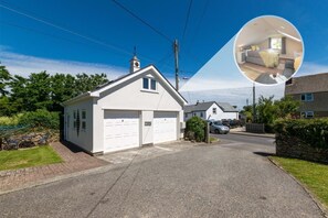 A residential property with a garage, a small attached shed, and a garden with a table and chairs. - 1 Bed in Padstow (oc-p00035) (Saint Merryn)