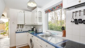 Een compacte keuken met witte kastjes, een wasmachine, een gootsteen en een kookplaat.